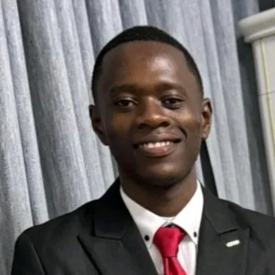 Portrait de Jenovic (Joe) Kanyimb Tshinyam en costume noir et cravate rouge.